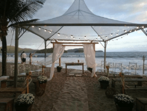 Tenda transparente com luminarias decorando um ambiente de casamento na praia