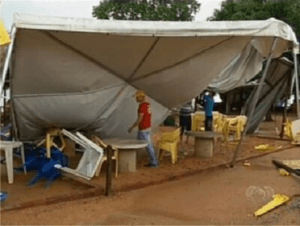 Tenda branca cobrindo mesas caidas no chão após chuva.